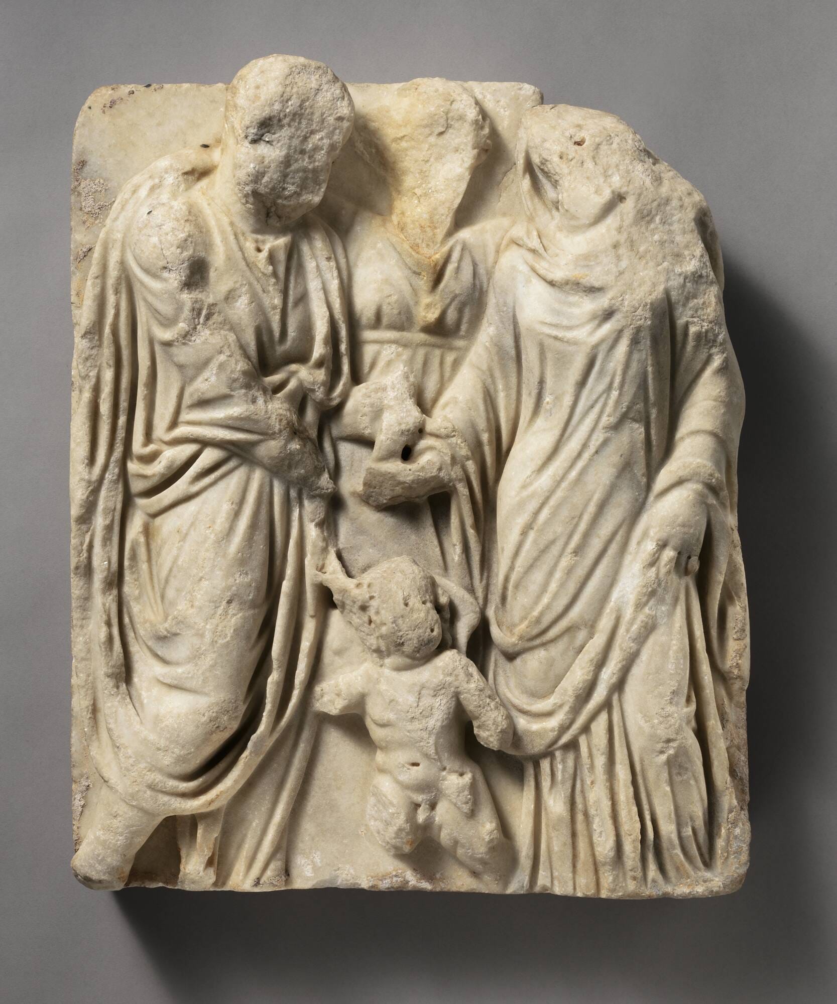 Marble sarcophagus fragment: Marriage scene of a man and a woman clasping hands, a figure between them and Eros below.