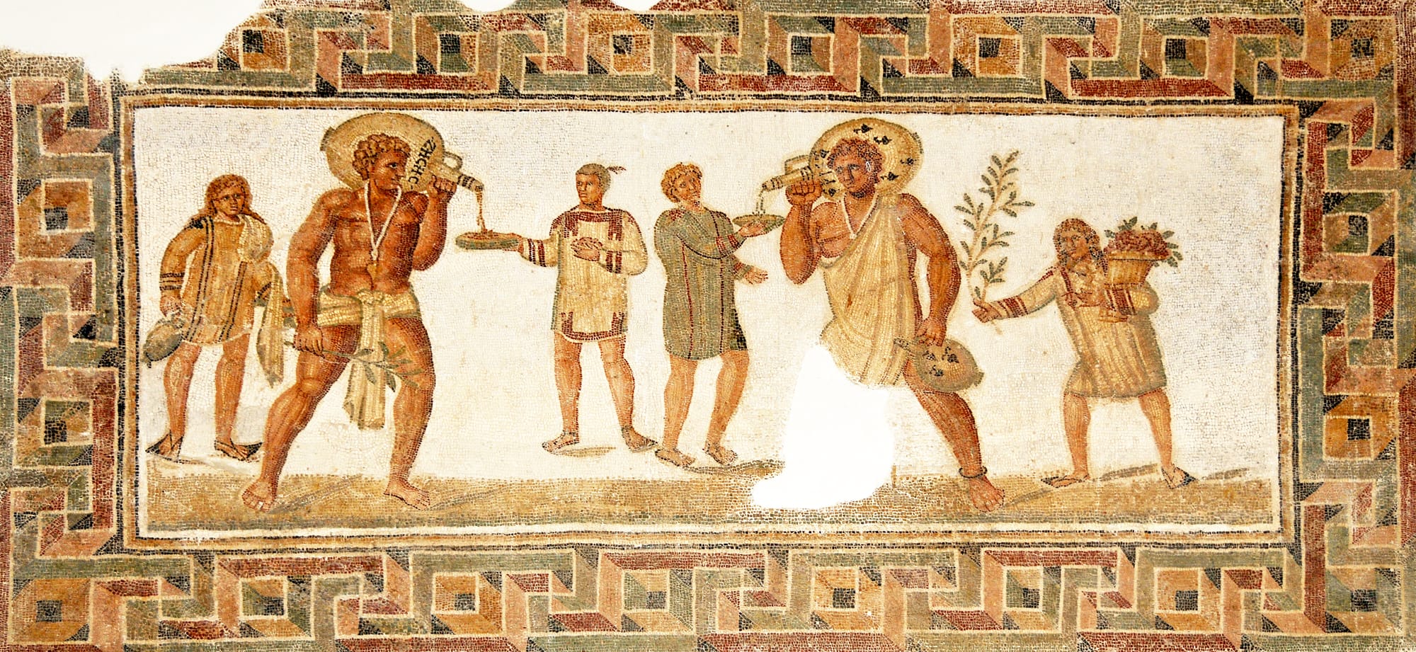 Roman mosaic from Dougga, Tunisia (2nd/3rd century AD): two large slaves carrying wine jars each wear an amulet against the evil eye on a necklace, with one in a loincloth (left) and the other in an exomis;the young slave to the left carries water and towels, and the one on the right a bough and a basket of flowers. 