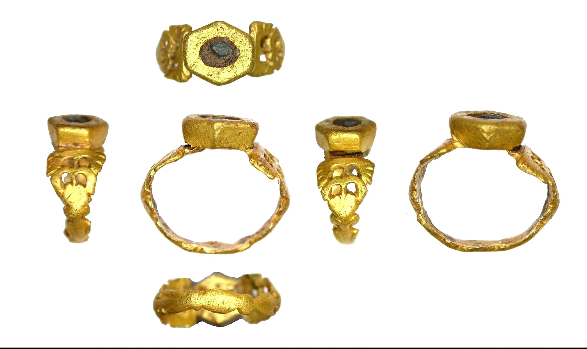 A tiny Roman gold finger-ring, intact and un-damaged. The hexagonal hoop has neatly-incised decorative edges and triangular shoulders with elaborate openwork. The small hexagonal box bezel, with sloping sides and flat surface, is set with a tiny oval gem, its surface now degraded. The remaining fragment of original surface appears black in colour and appears to retain part of an engraved design. Date: 3rd - 4th century AD.